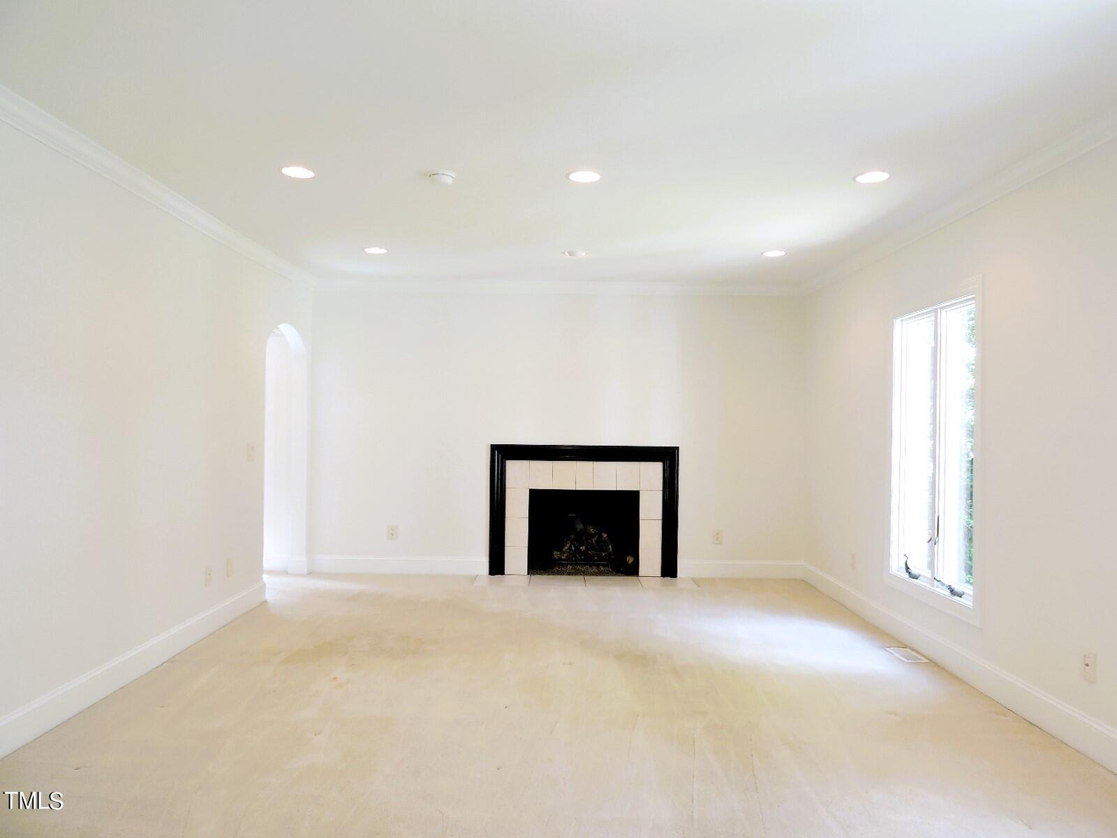 Empty living room with a tiled fireplace, recessed lights, and a tall window.