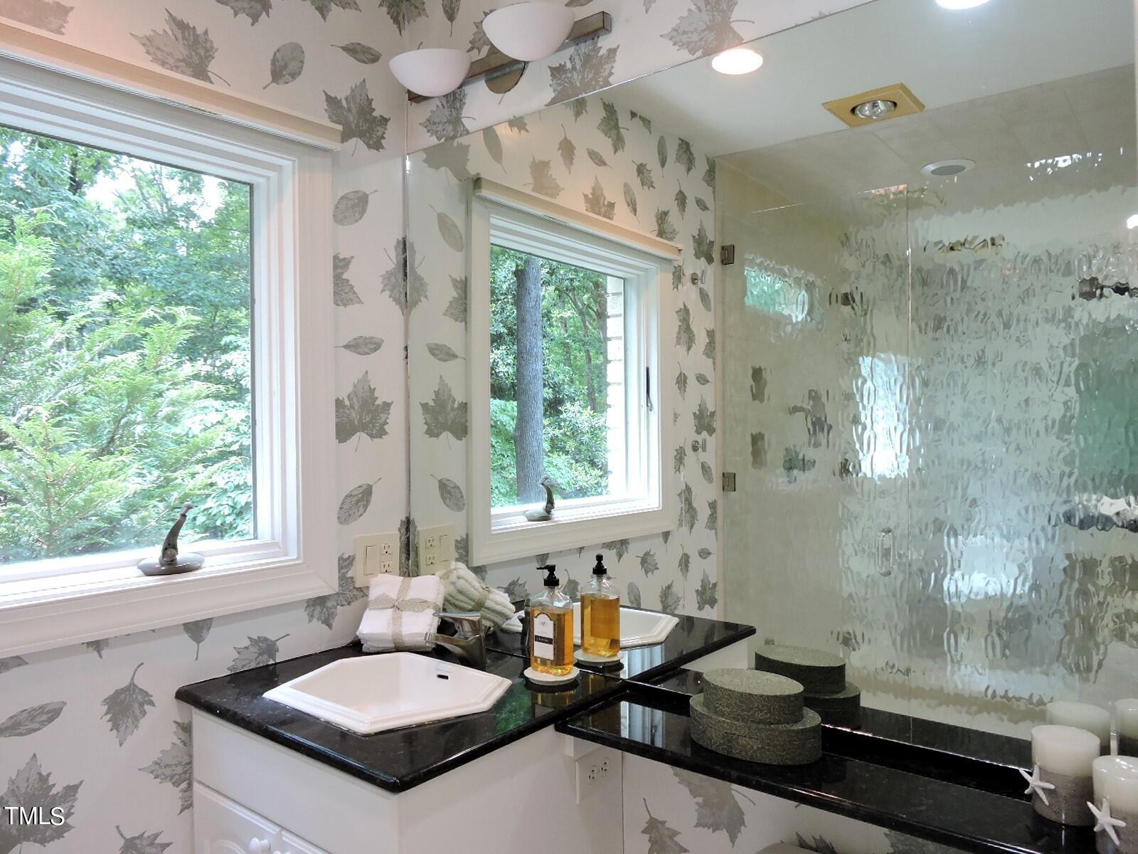 Bathroom with leaf-patterned wallpaper, black vanity counters, and a textured glass shower.