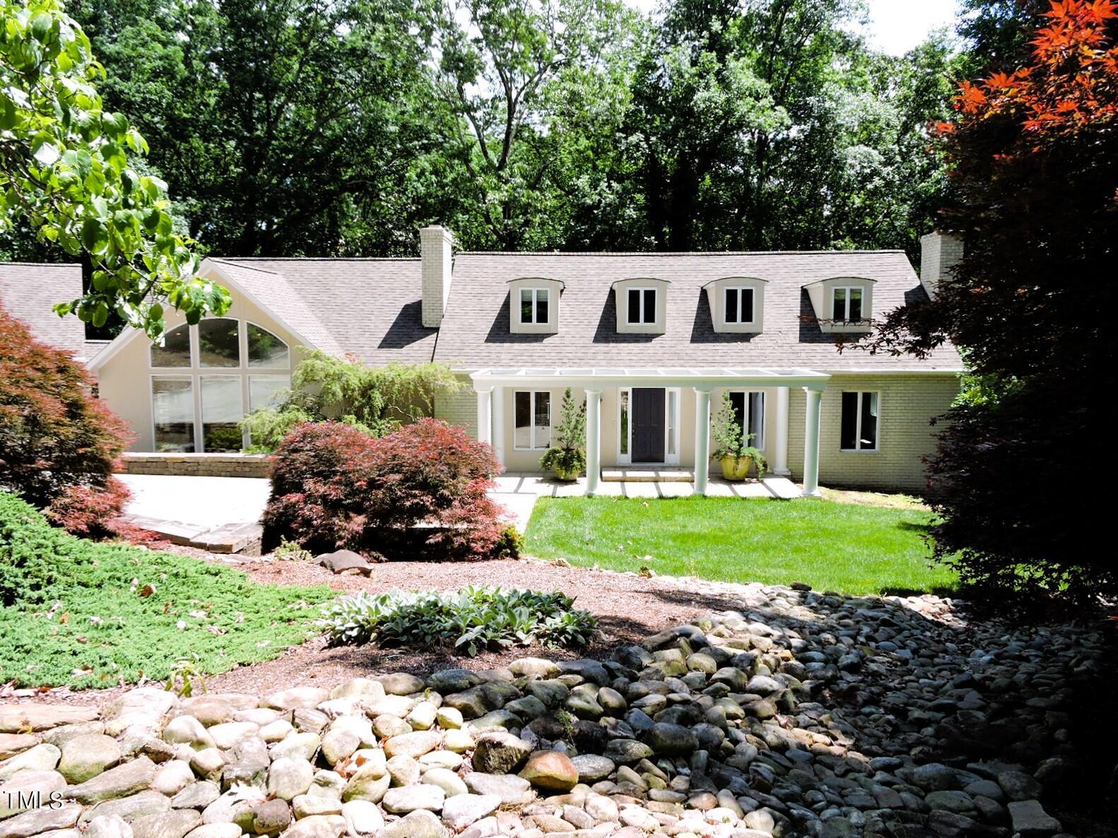Light-colored home with dormer windows, a columned entrance, and a landscaped stone creek bed.