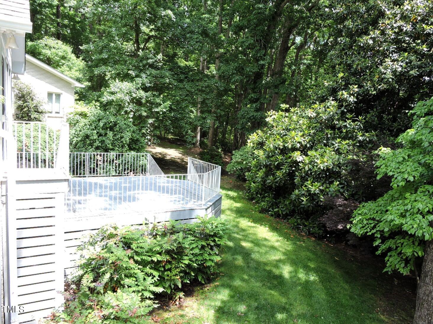 White-sided home and raised deck with white railings in a wooded backyard.