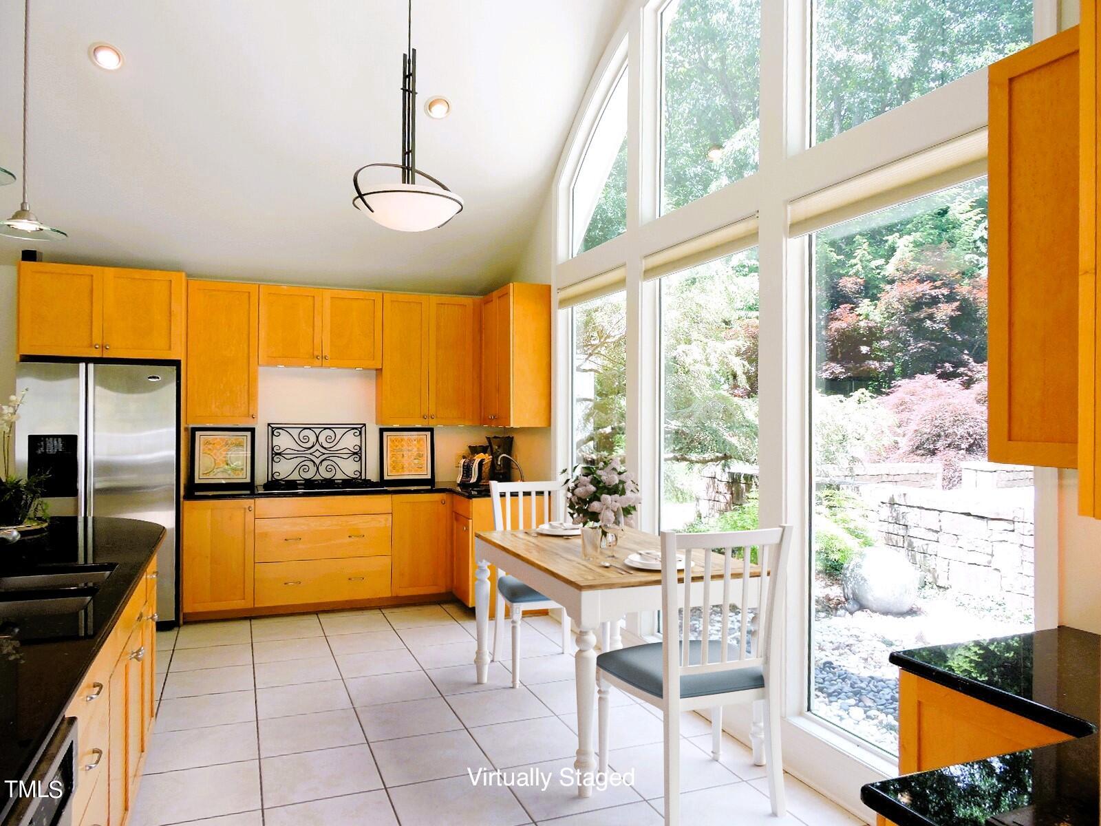 Kitchen with honey-colored cabinetry, a small dining table, and tall garden-facing windows.