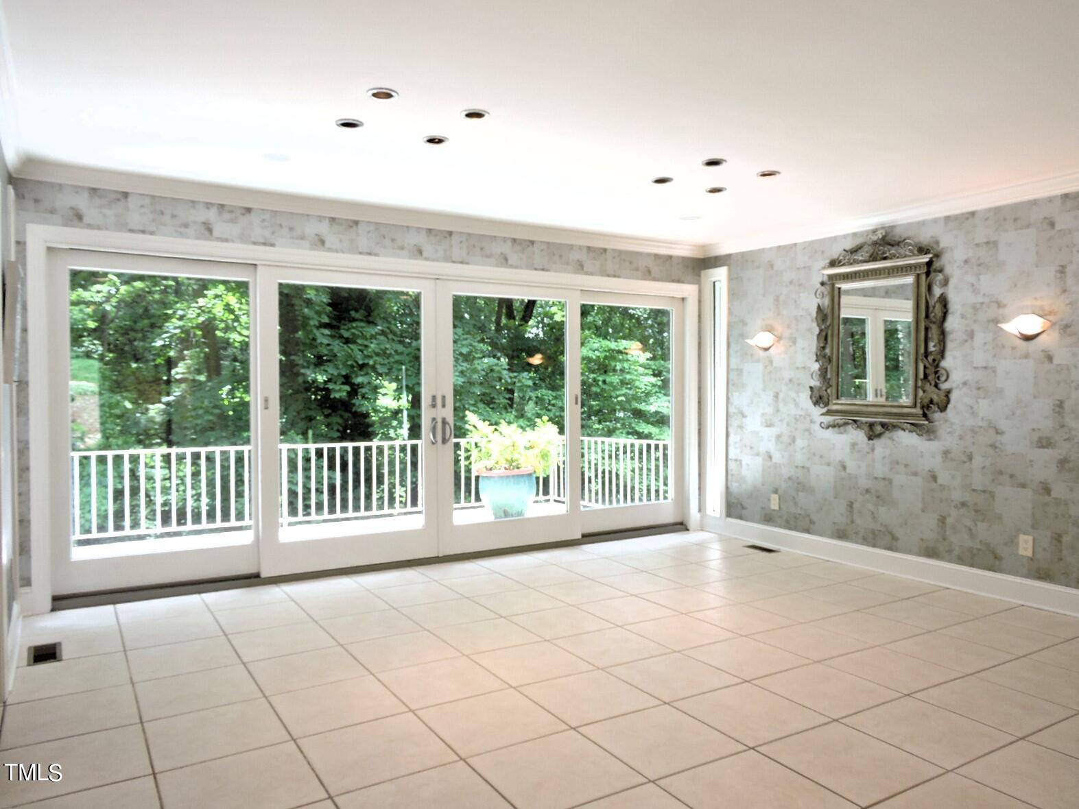 Empty tiled sunroom with wide sliding glass doors opening onto a wooded deck.