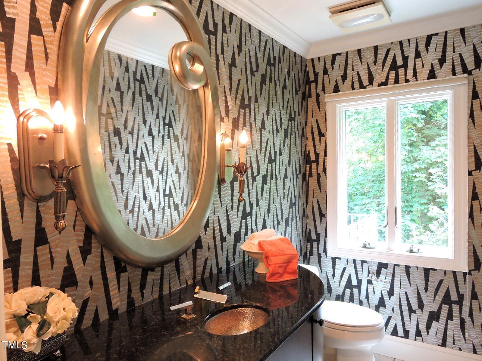 Powder room with geometric wallpaper, an oversized oval mirror, brass sconces, and a dark vanity.