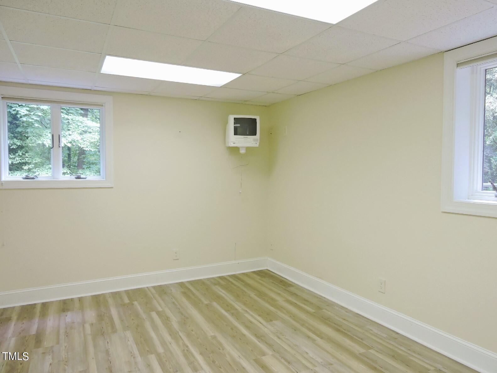 Empty room with light wood-look flooring, two windows, and a wall-mounted television.