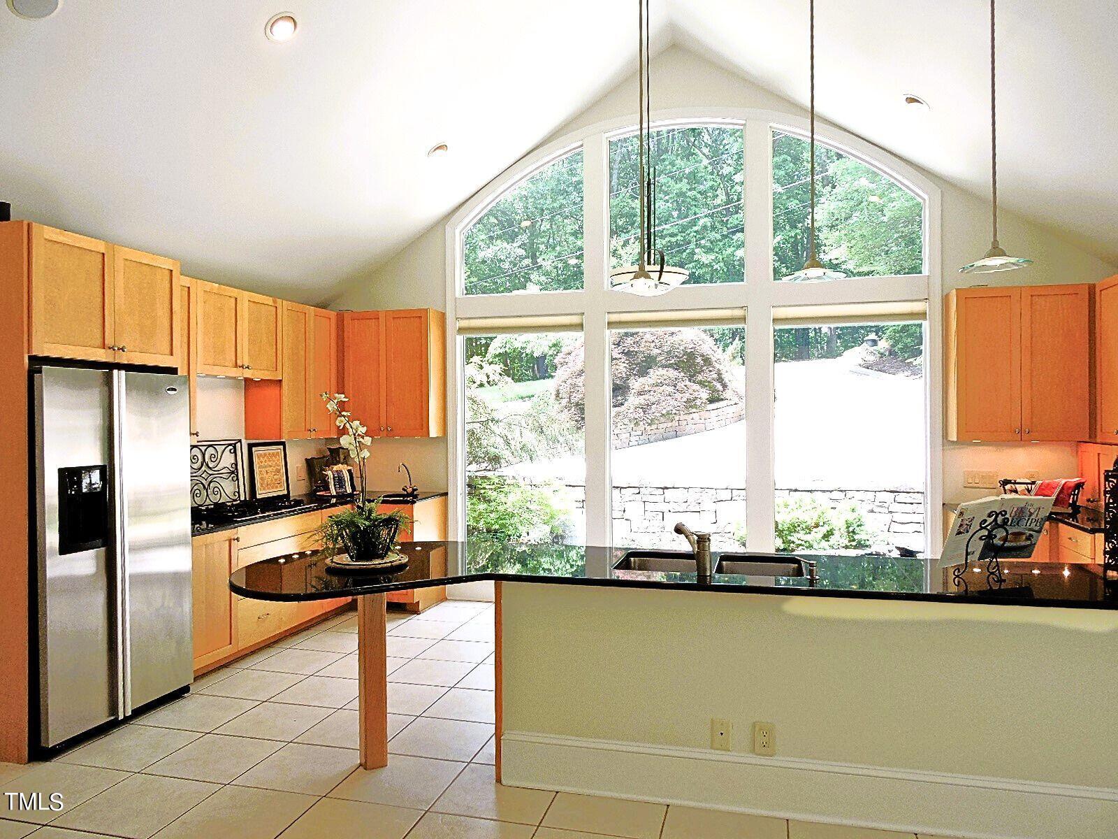 Kitchen with warm wood cabinets, a black island, and tall arched windows overlooking trees.