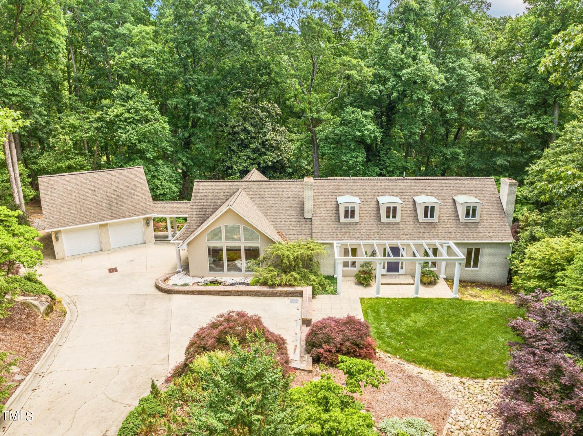 Large home with four dormers and a glass-fronted gable, surrounded by trees and landscaped grounds.