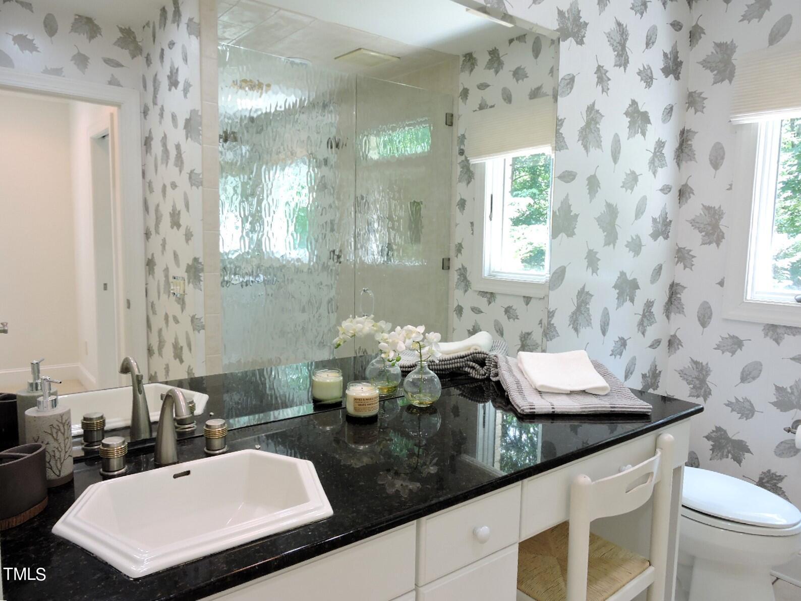 Bathroom with a black vanity, glass shower, and distinctive gray leaf-patterned wallpaper.