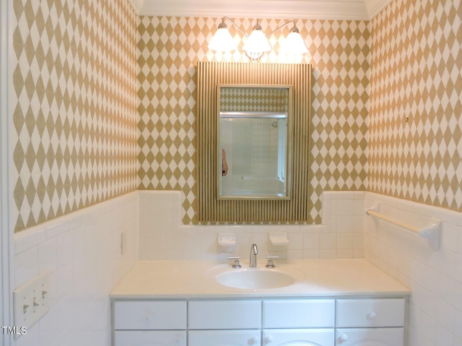 Bathroom vanity with a framed mirror and beige-and-white diamond-pattern wallpaper.