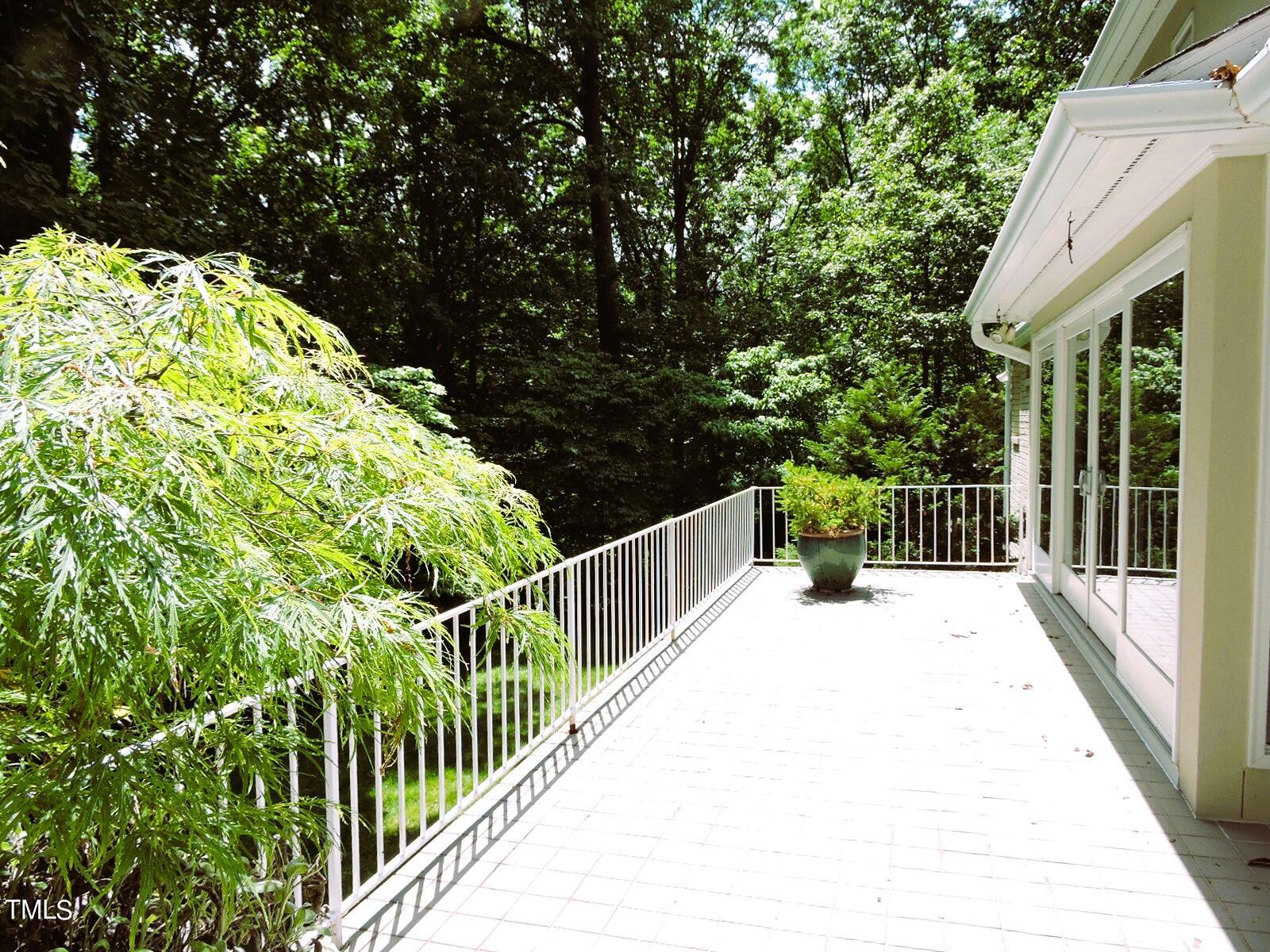 Tiled patio with white railings and sliding glass doors beside dense woods.