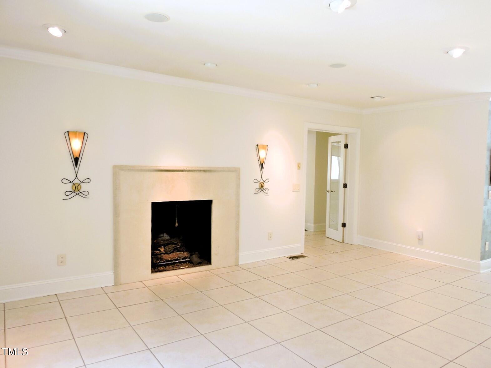 Empty room with a stone fireplace, decorative wall sconces, and pale tile flooring.