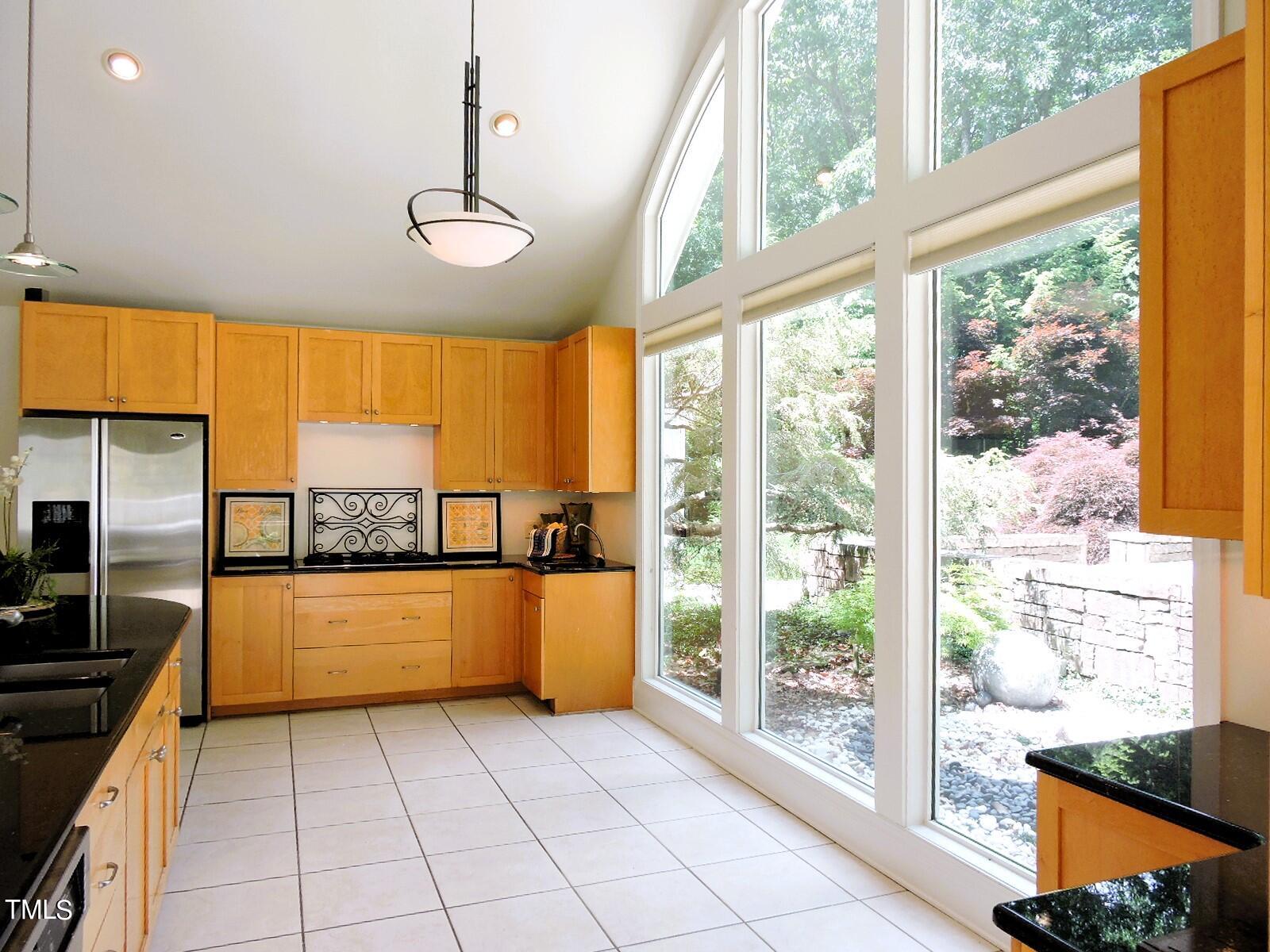 Kitchen with honey-colored cabinets, black countertops, and tall windows overlooking a garden.