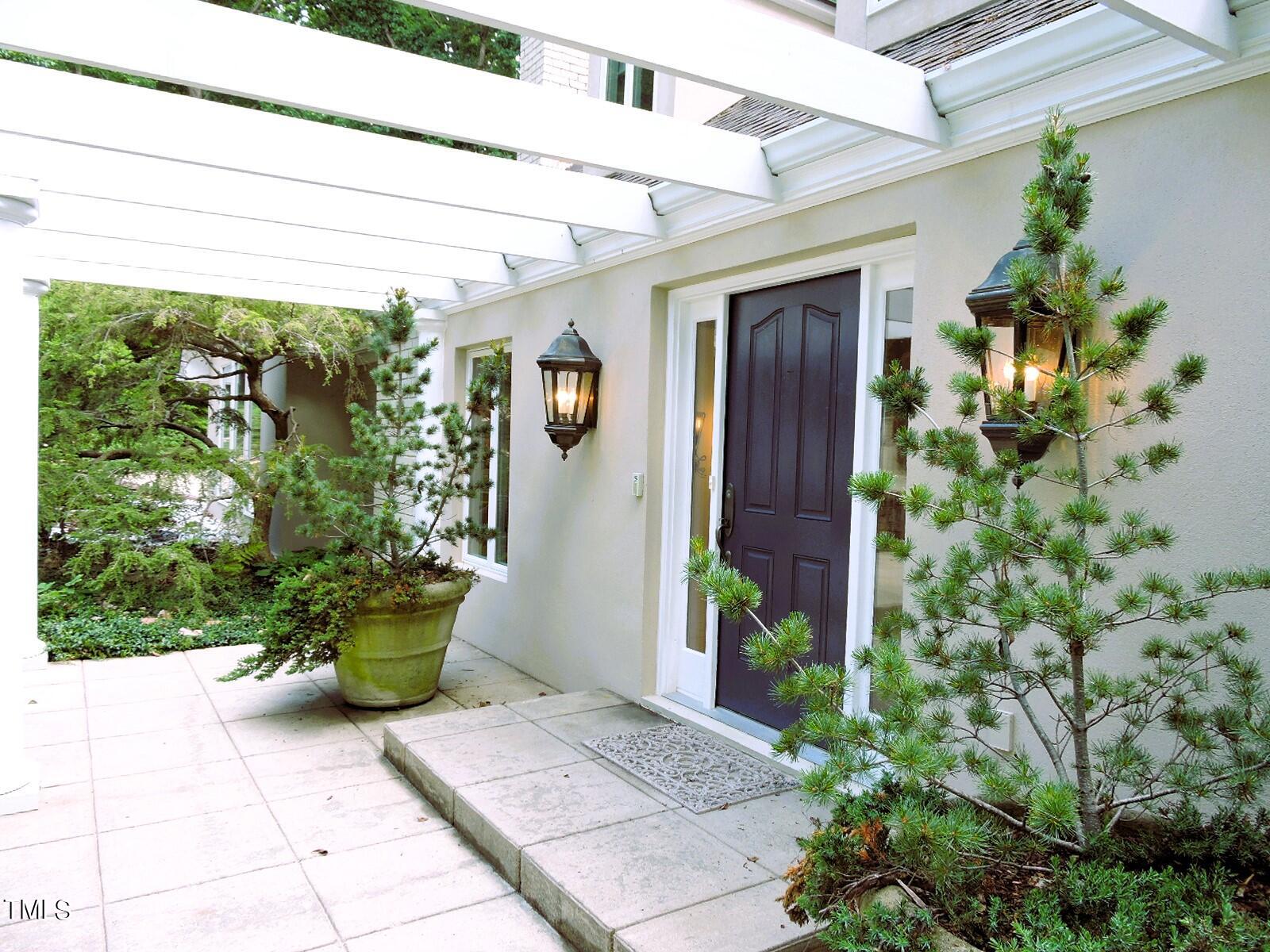 Home entrance beneath a white pergola, with a dark front door and landscaped stone walkway.