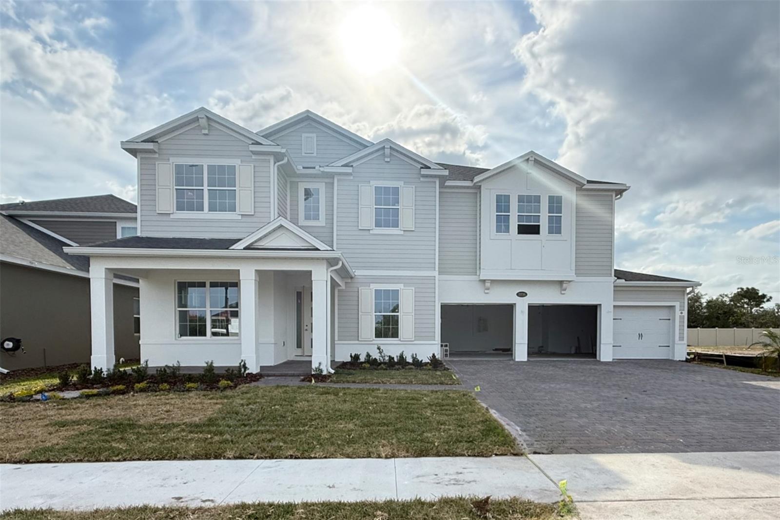 Two-story gray-and-white house with a covered porch, open garage bays, and a wide paved driveway.