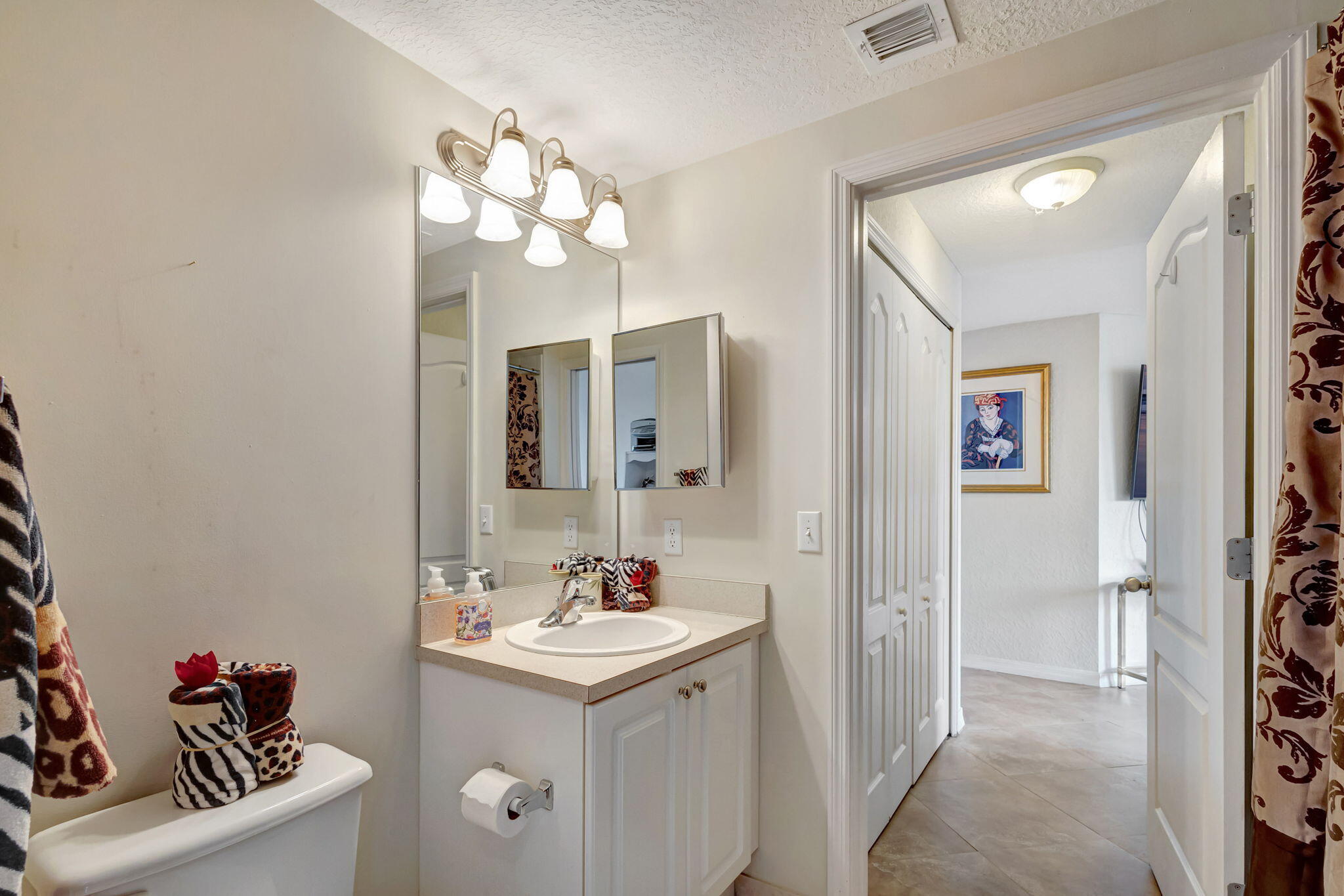 Bathroom with a single-sink vanity and mirror beside an open doorway to a tiled hall.