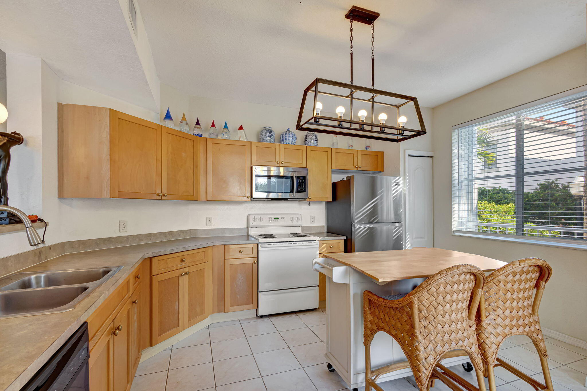 Kitchen with light wood cabinets, stainless refrigerator, and a breakfast island with woven bar stools.