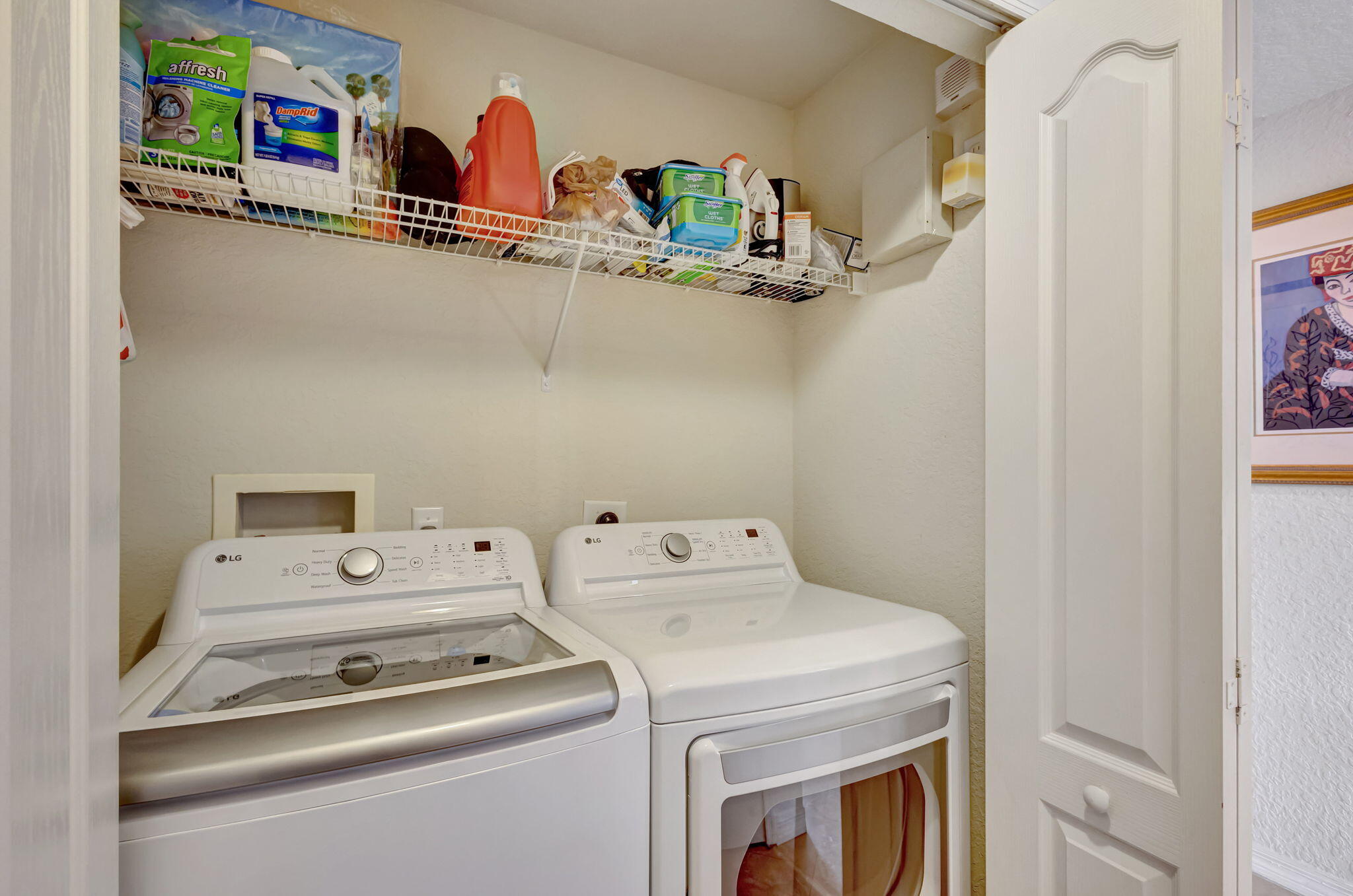 Laundry room with a white washer and dryer beneath a shelf of cleaning supplies.