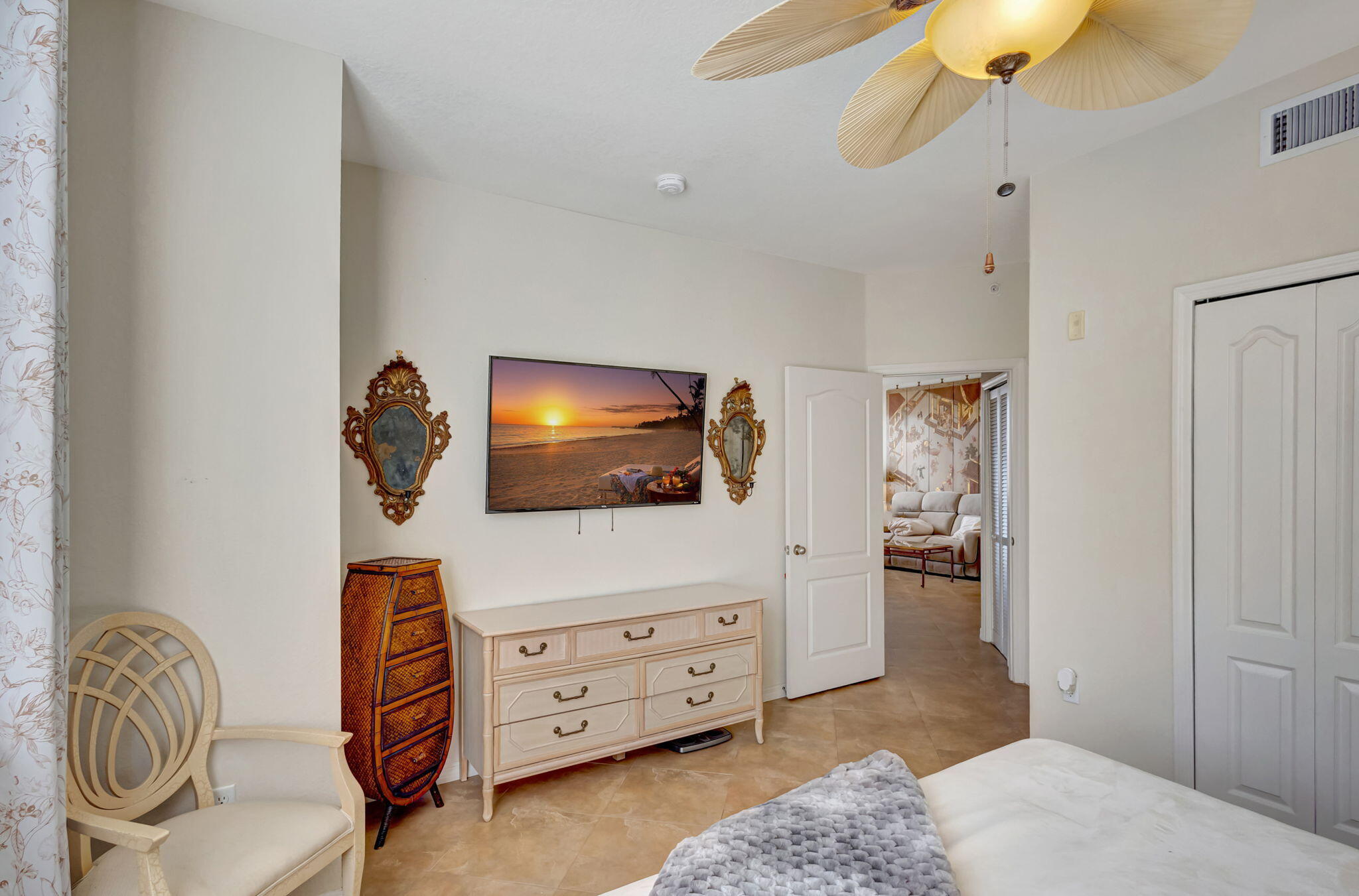 Furnished bedroom with a carved cream dresser, wicker chest, and open doorway to a sitting area.