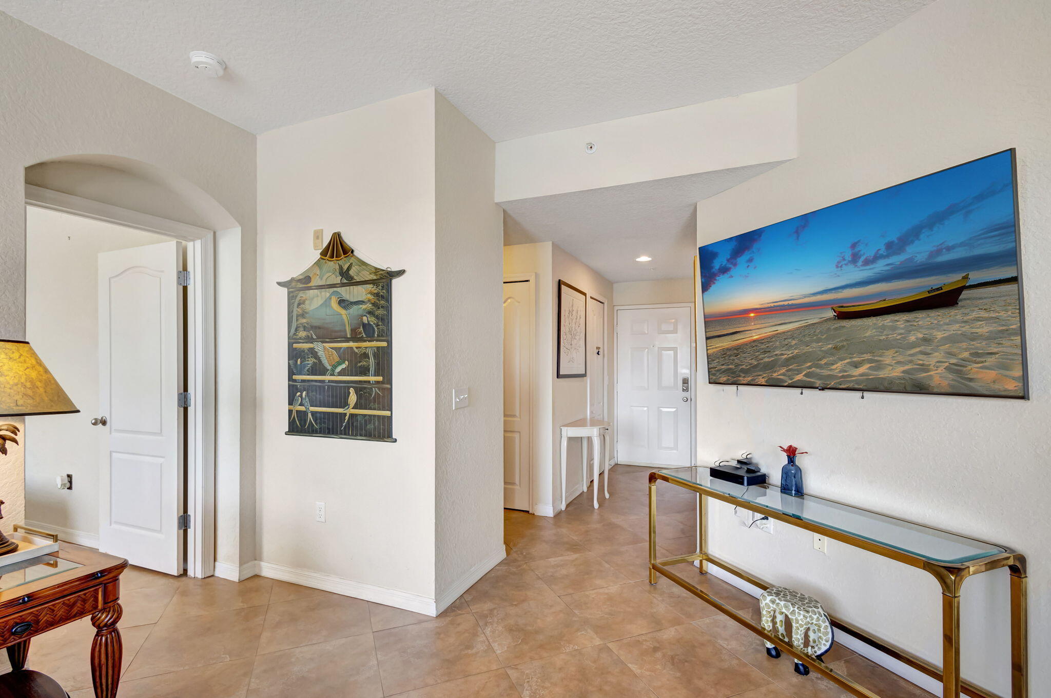 Condo entryway with tiled floors, a glass-and-brass console, and beach sunset artwork.