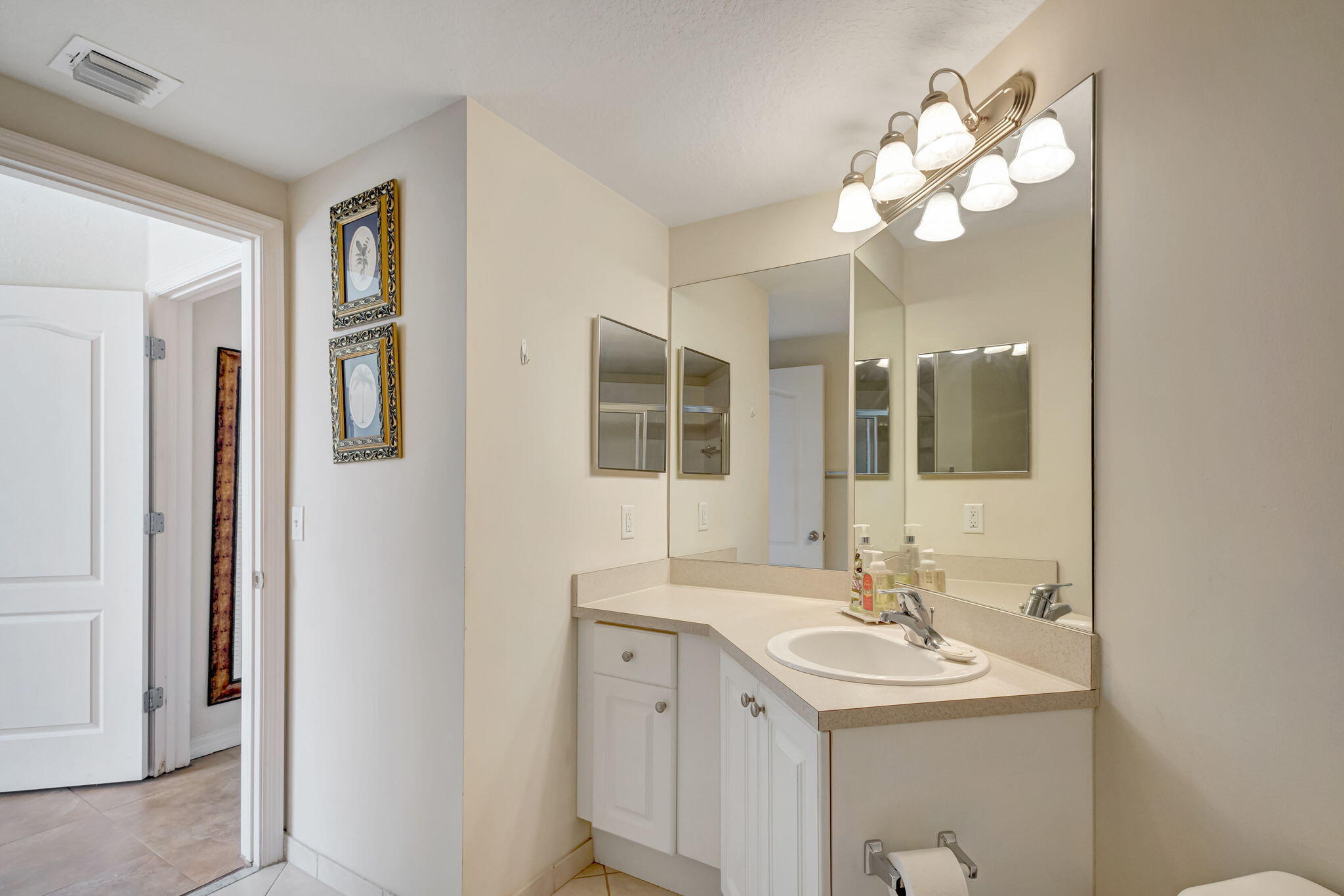 Bathroom vanity with an oval sink, expansive mirrors, and a bright multi-light fixture.