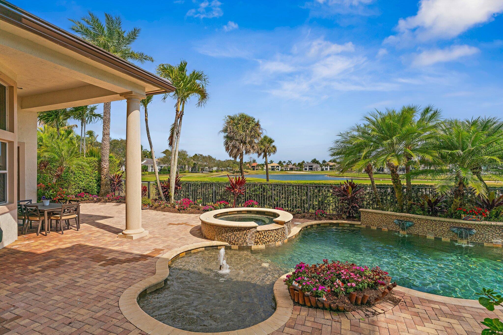 Backyard pool and raised spa overlook the water, framed by palms and a covered patio.