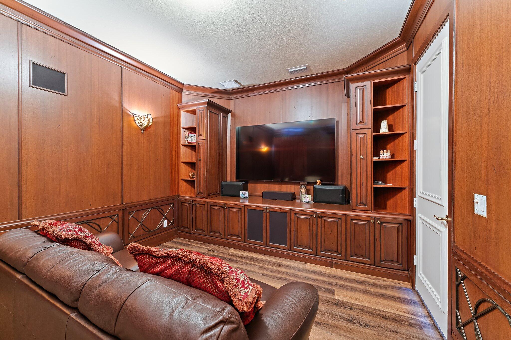 Wood-paneled home theater with a large television and brown leather sectional sofa.
