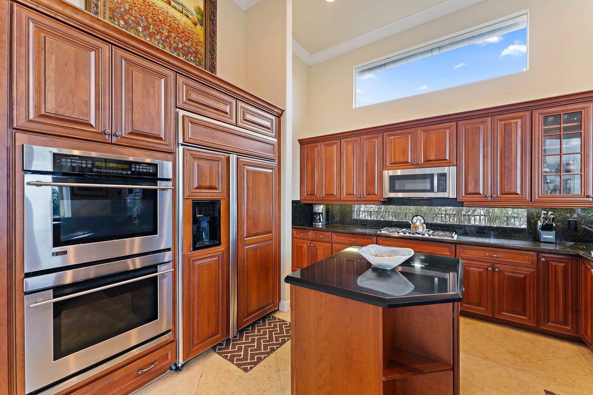 Kitchen with dark wood cabinets, stainless-steel double ovens, black counters, and a central island.