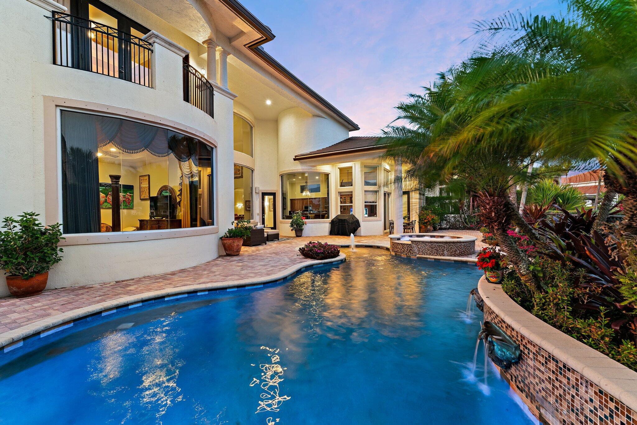 Curved backyard pool and spa beside a two-story stucco home at dusk.