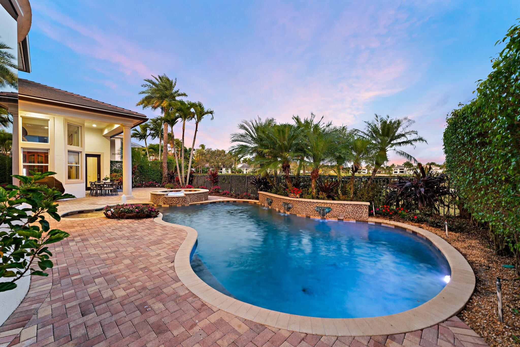 Curved backyard pool and spa beside a paver patio, framed by palms at dusk.