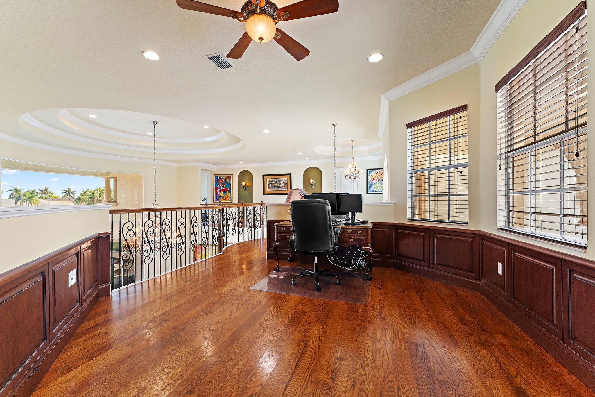 Upstairs home office with hardwood floors, dark wood paneling, desk, and ornate railing overlooking the lower level.