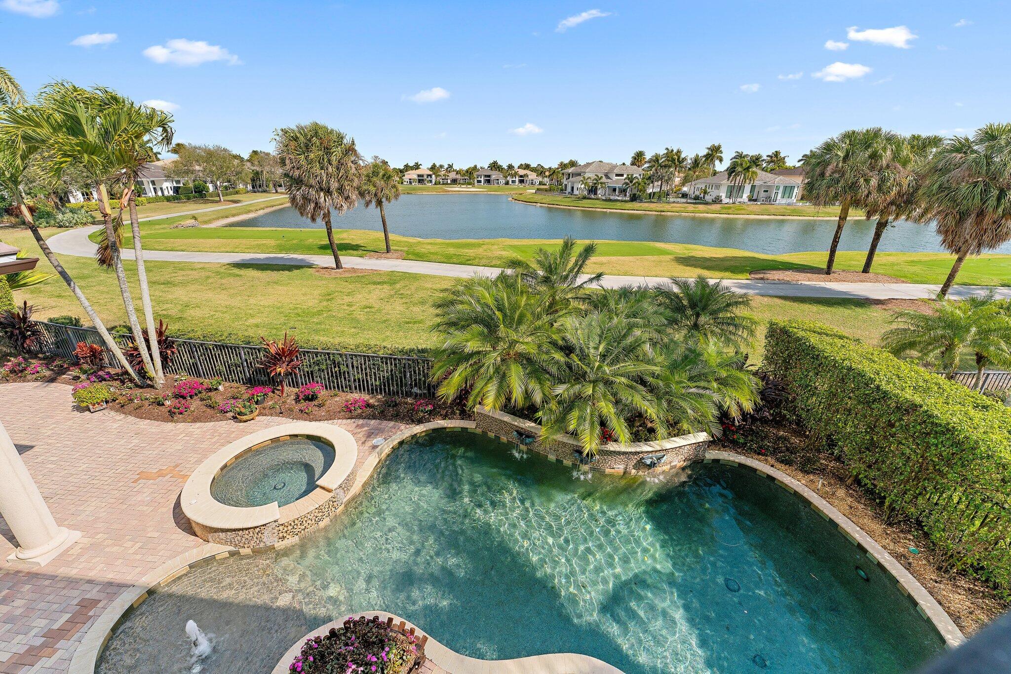 Backyard pool and round spa overlook a lake, with a brick patio and palm landscaping.