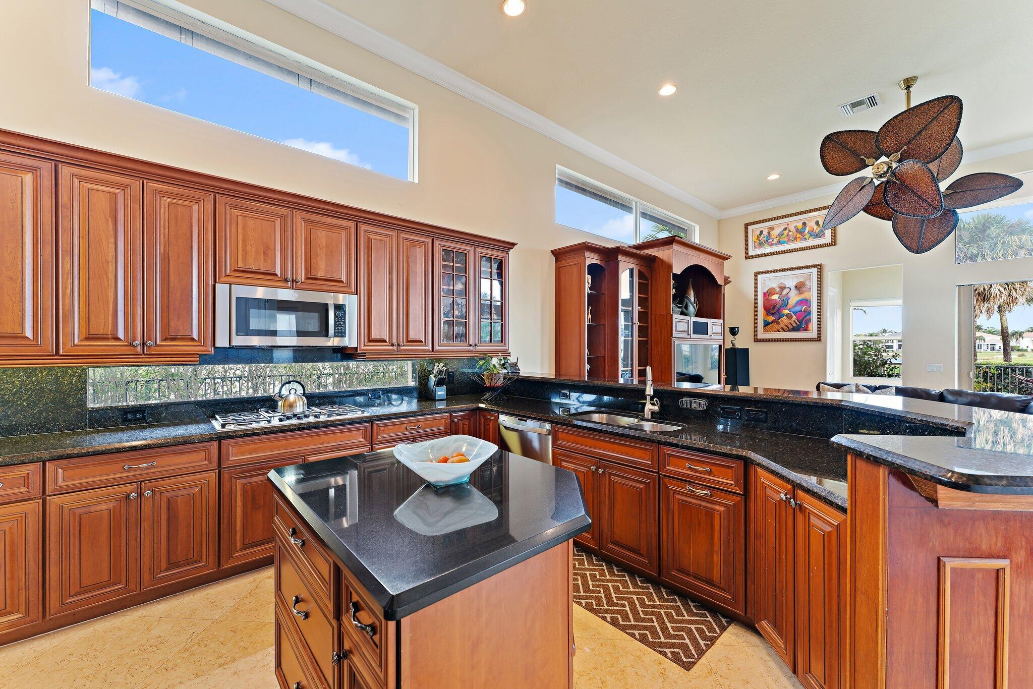 Kitchen with rich wood cabinets, black granite counters, a central island, and high clerestory windows.