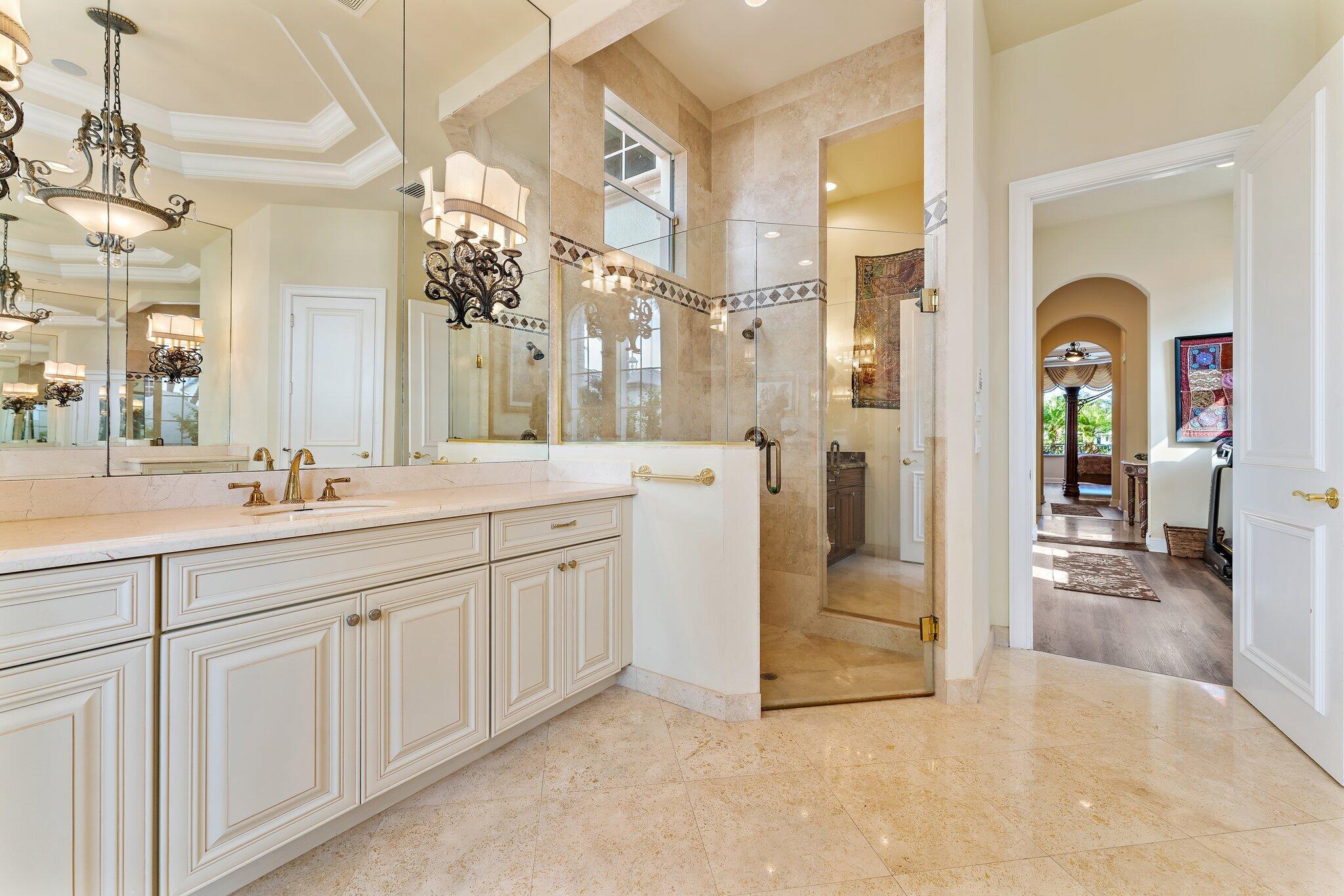 Primary bathroom with a long white vanity, mirrored walls, and a glass-enclosed stone shower.