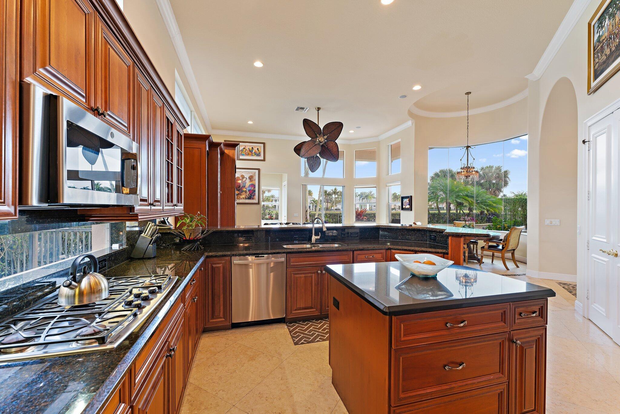 Kitchen with rich wood cabinetry, a large island, black granite counters, and windows overlooking palm trees.