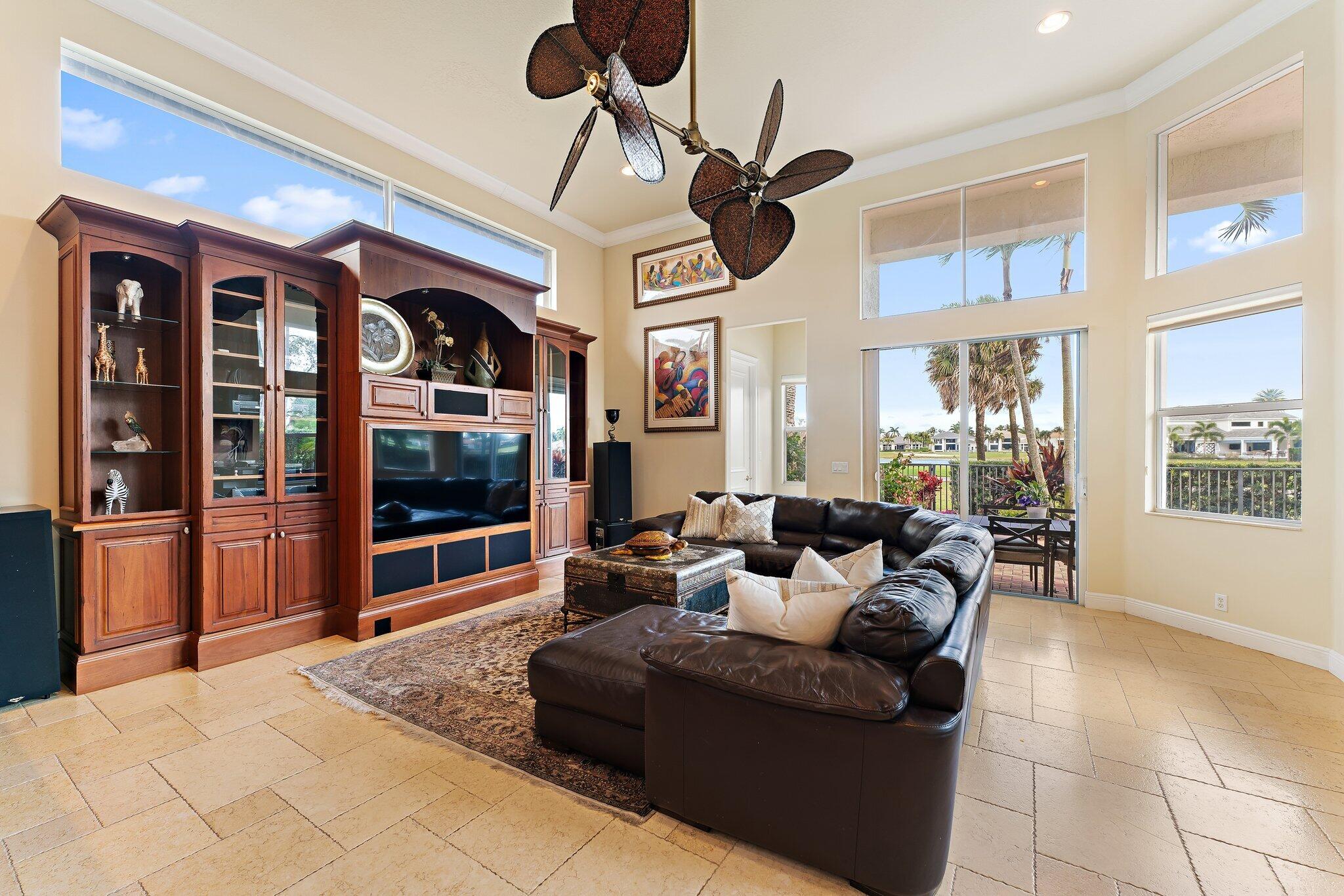 Living room with a leather sectional, built-in wood entertainment center, and large windows overlooking palm trees.