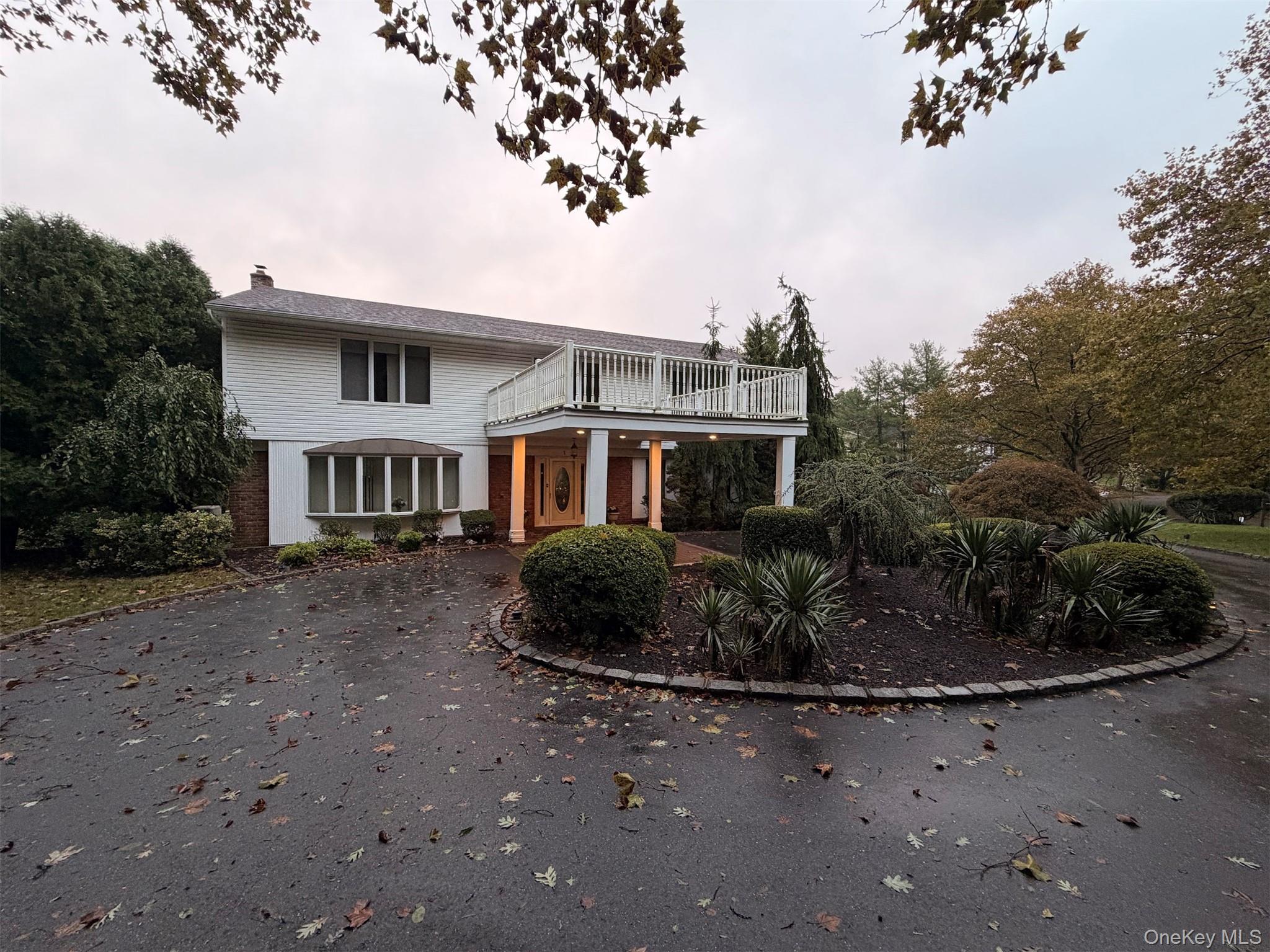 Two-story home with a raised deck, covered entrance, landscaped garden, and broad driveway.