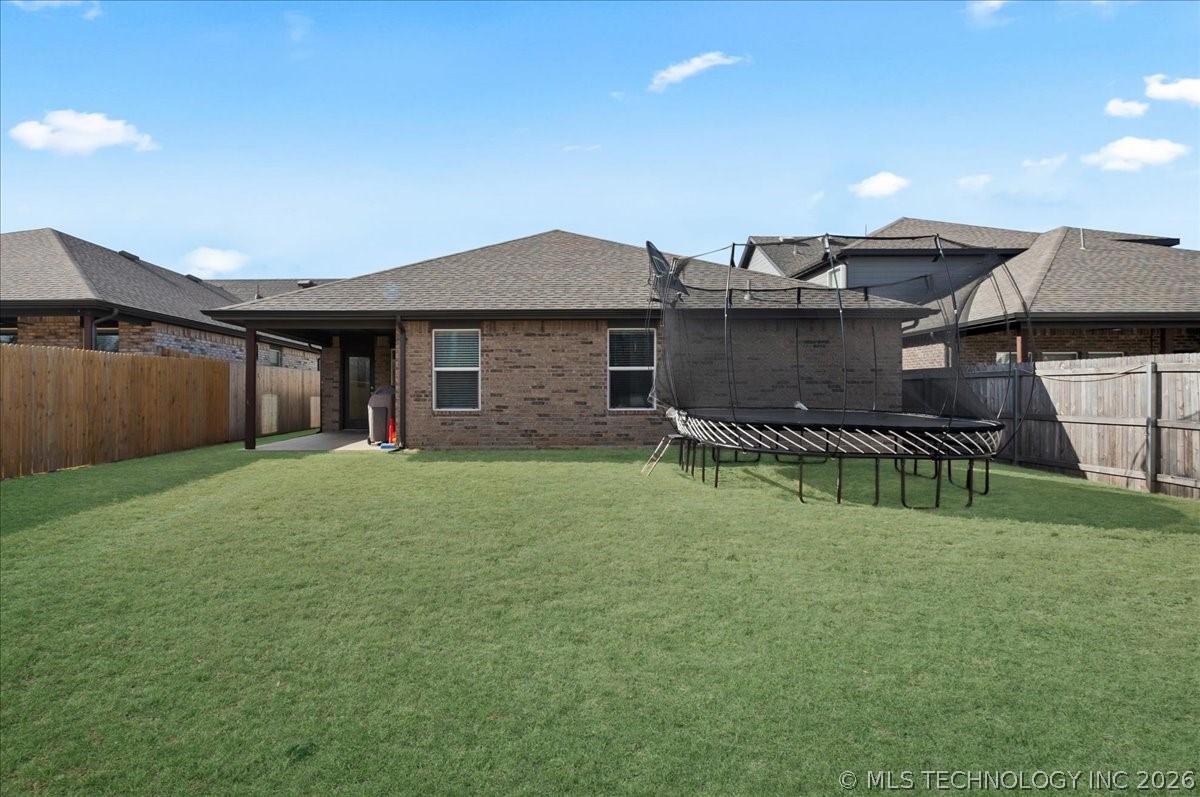 Rear exterior of a brick home with a fenced lawn, covered patio, and trampoline.