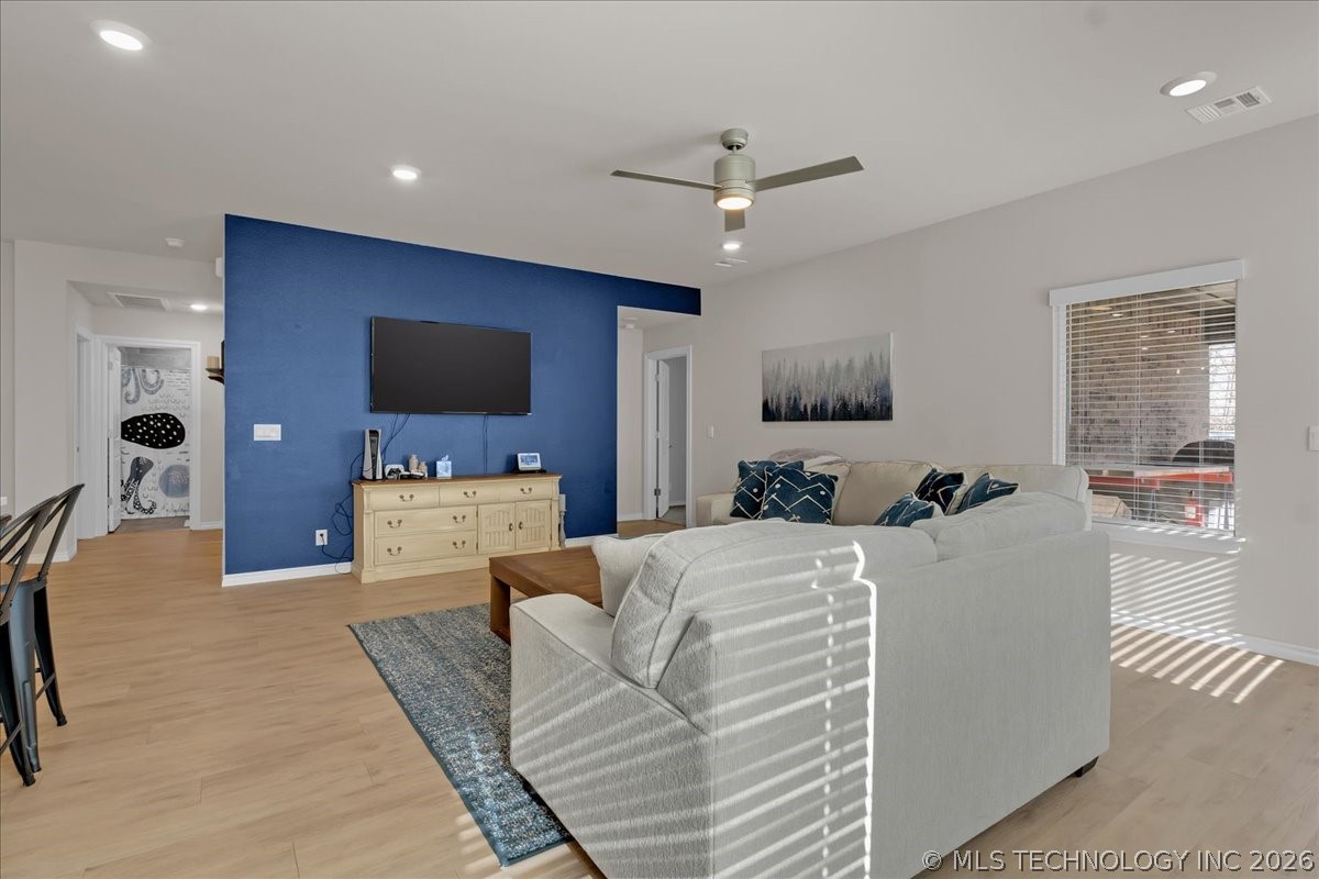 Living room with a white sectional, blue accent wall, mounted TV, and light wood flooring.