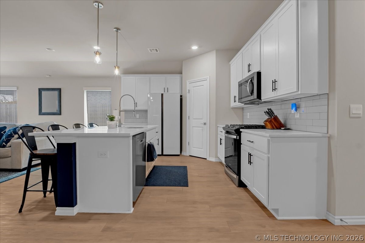 Open kitchen with white cabinets, stainless steel appliances, and a large island with a dark blue accent panel.