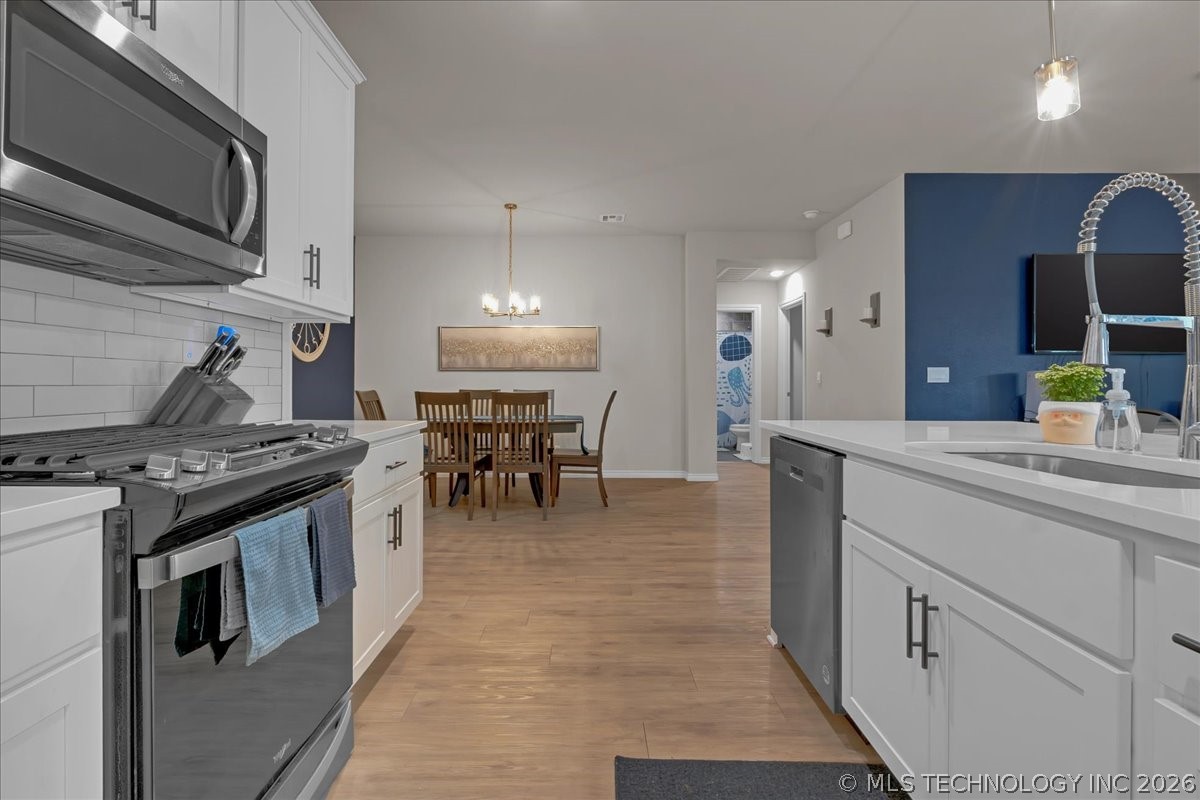 Open-plan kitchen with white cabinetry, stainless steel appliances, and an island facing a dining area.