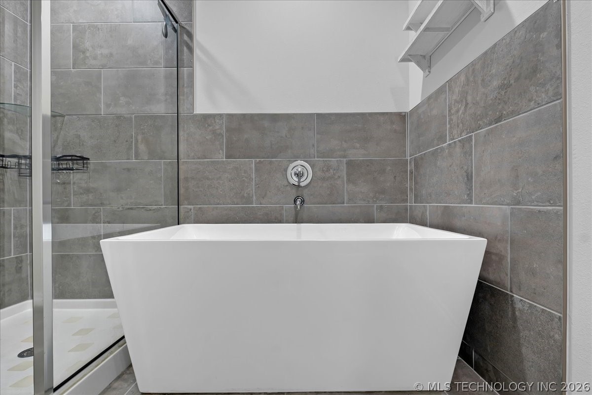 Bathroom with a white freestanding tub, gray tile walls, and an adjacent glass-enclosed shower.