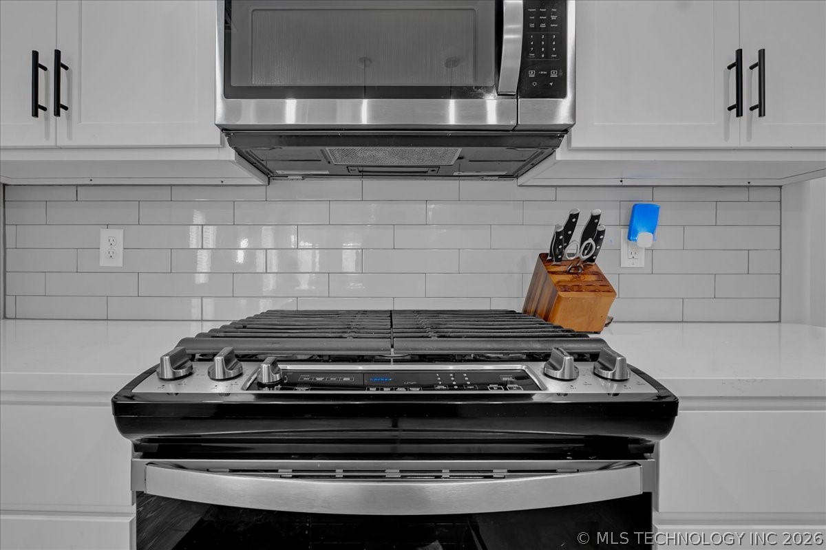 Kitchen with a stainless-steel gas range, microwave, and white subway-tile backsplash.
