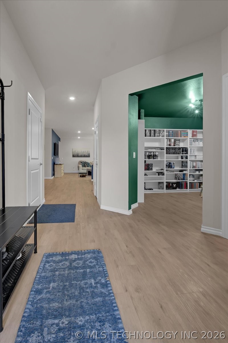 Hallway with blue rugs leads to a green room lined with built-in bookshelves.
