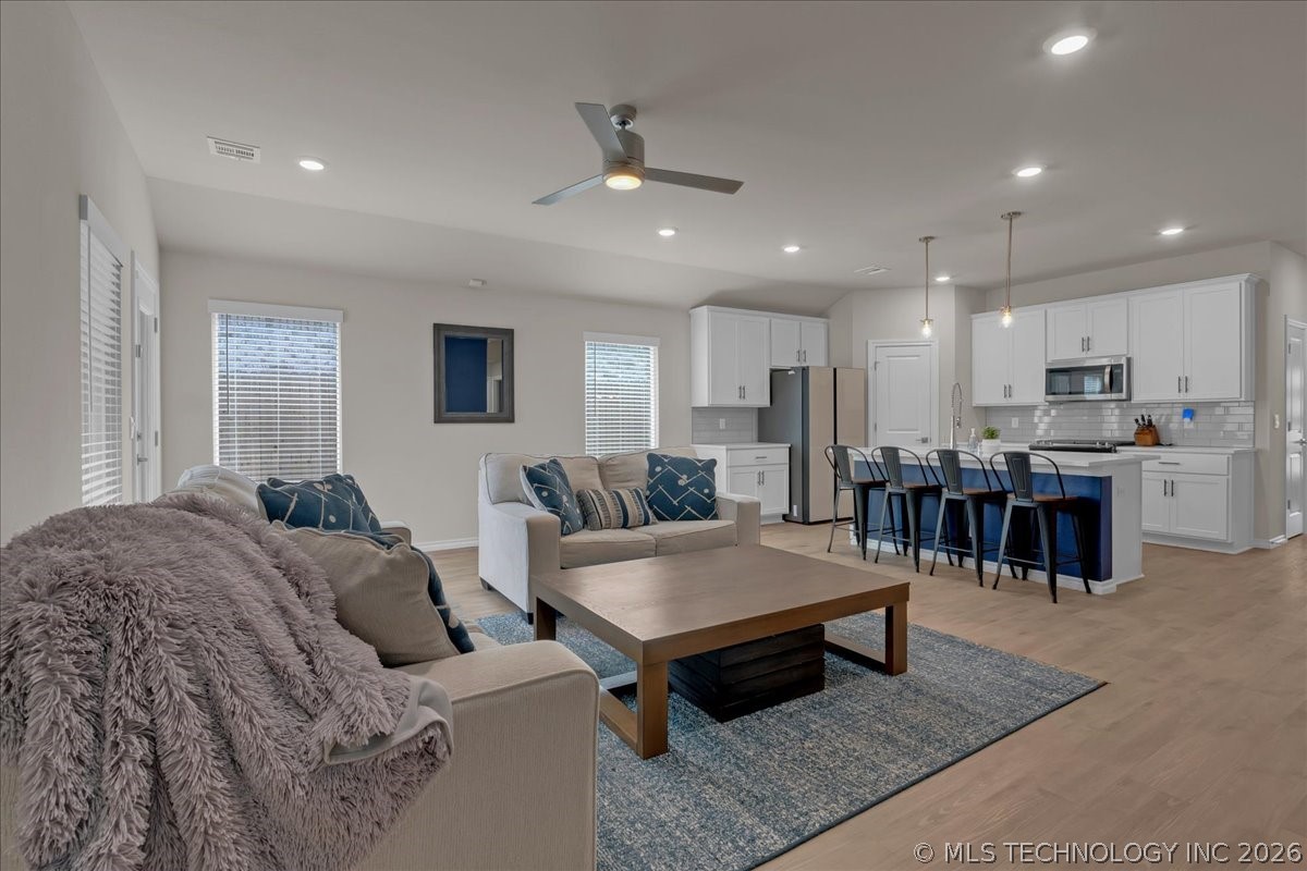 Open-plan living room and kitchen with a blue island, white cabinetry, and neutral seating.