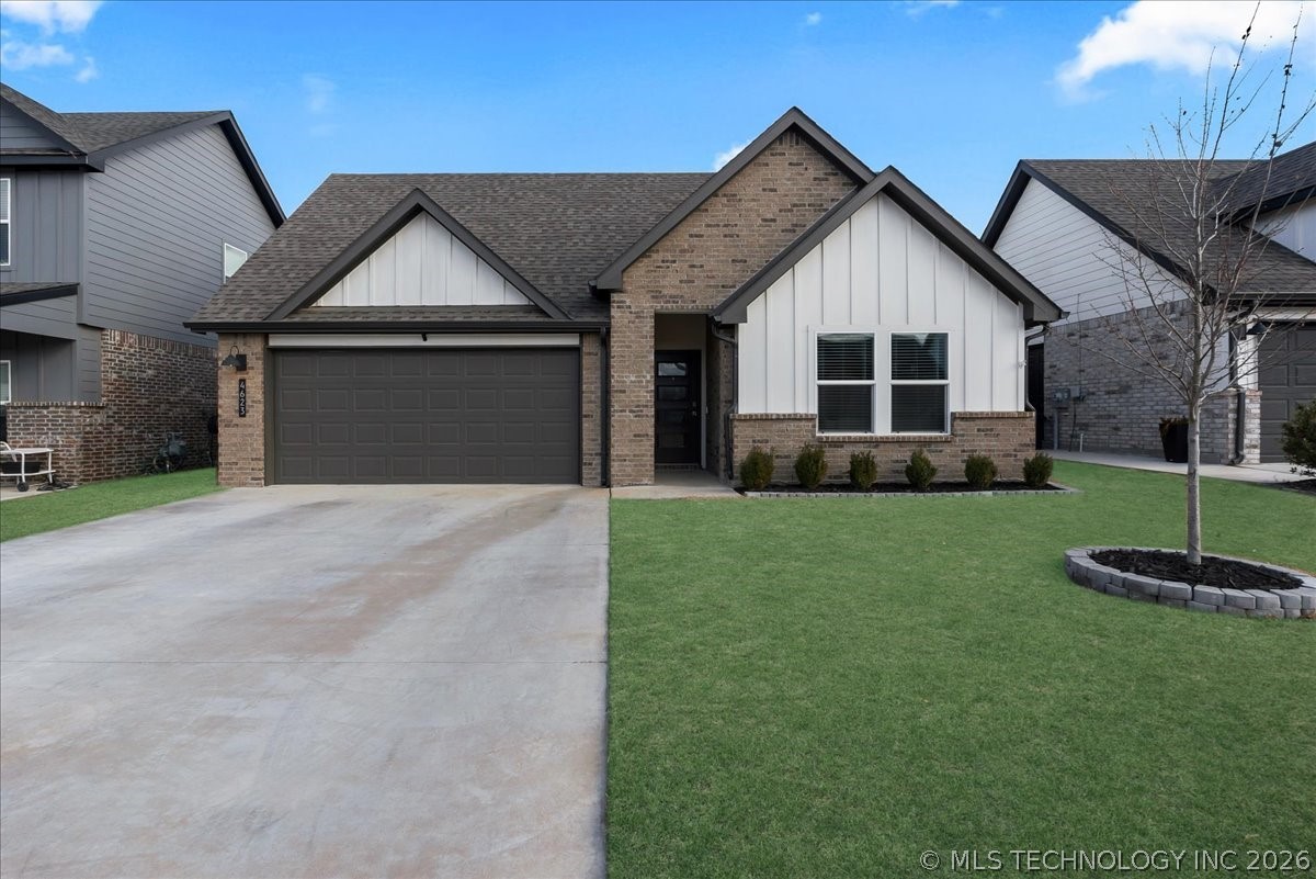 Single-story brick home with white gables, a dark garage door, broad driveway, and front lawn.