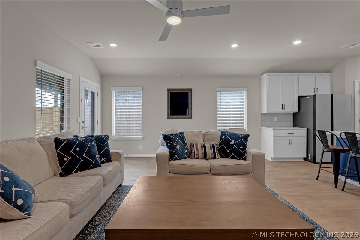 Living room with beige sofas, navy patterned pillows, a wood coffee table, and an adjoining white kitchen.