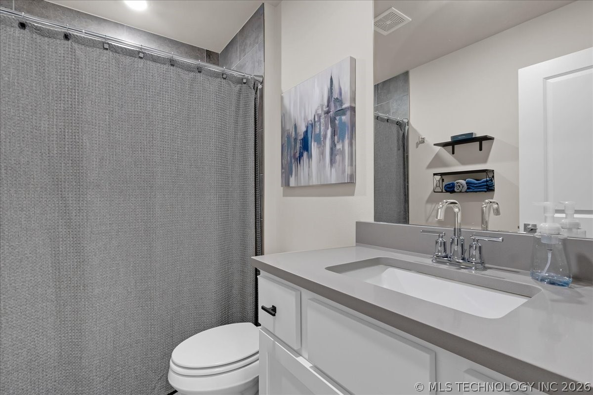 Bathroom with a gray shower curtain, white toilet, and vanity with a single sink and large mirror.
