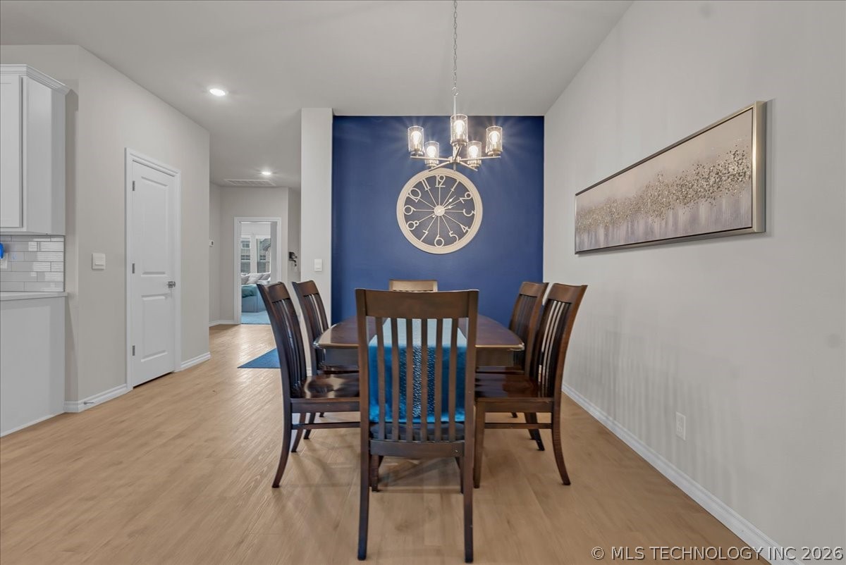 Dining room with a dark wood table, blue accent wall, oversized clock, and chandelier.