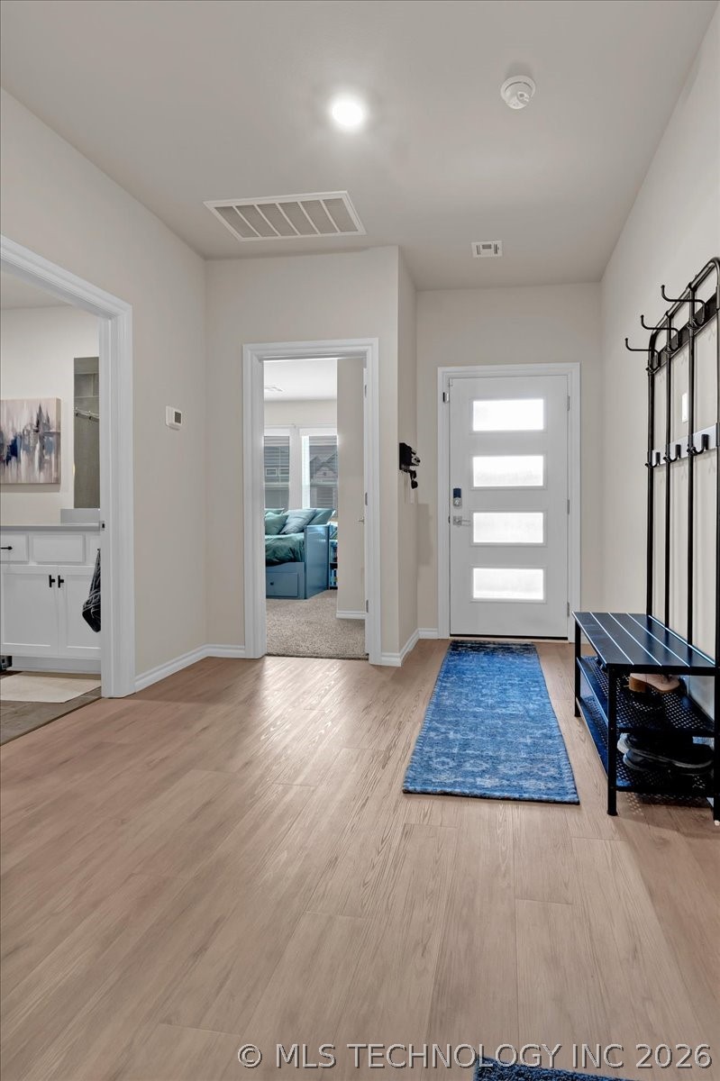 Entry foyer with light wood floors, a blue runner, and a white front door with frosted glass panels.