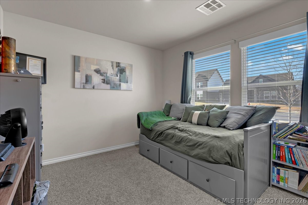 Bedroom with a gray drawer daybed, green bedding, and two large windows with blinds.