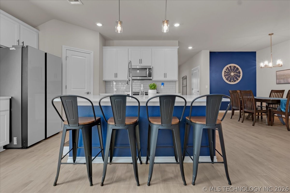 Kitchen with white cabinets, stainless appliances, and a blue island lined with four bar stools.
